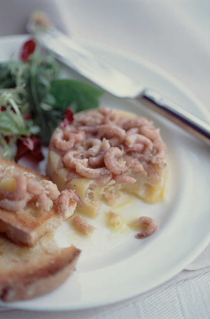 Vorspeise aus eingetopften Garnelen auf Sauerteigtoast mit Salatbeilage auf einem weißen Teller mit Messer