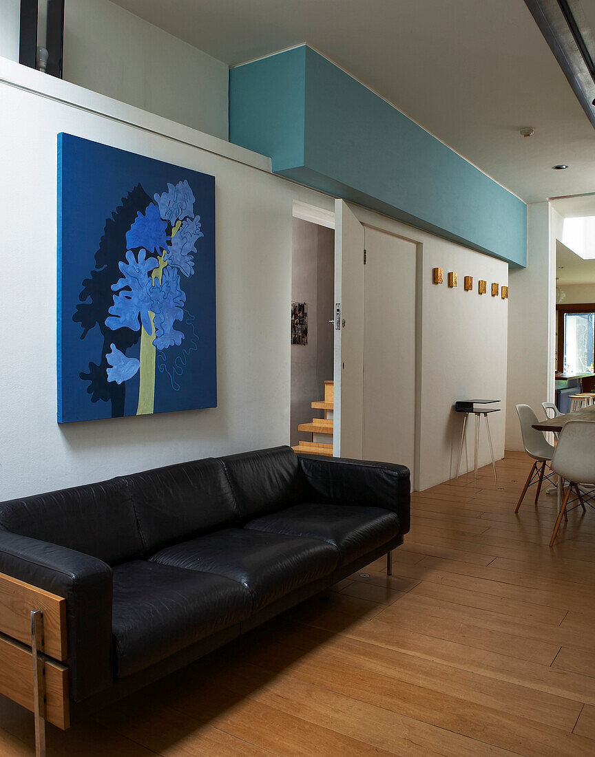 Black leather sofa and colourful floral canvas in open plan living area with door to stair