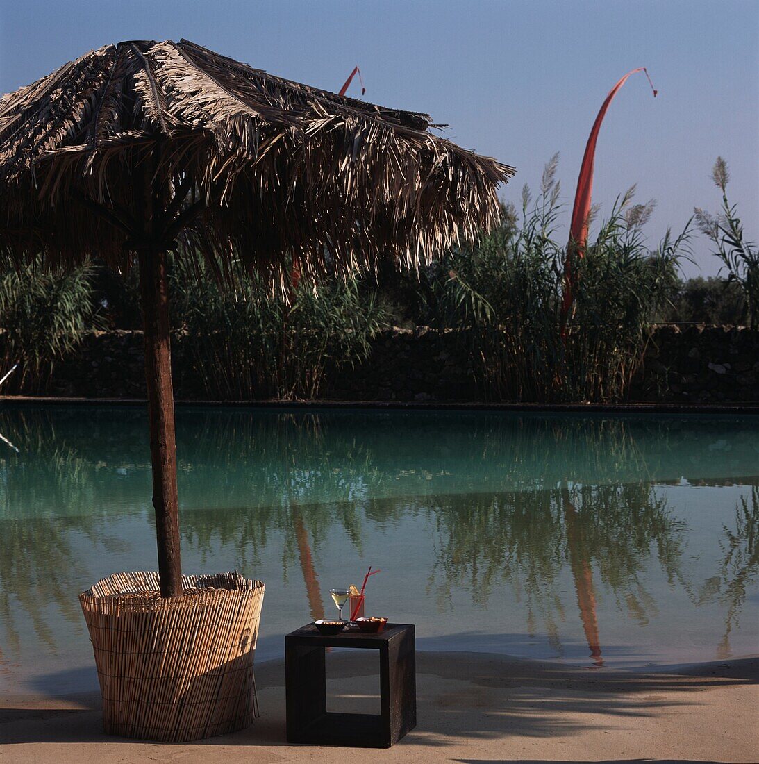 Cocktails under sunshade made of dry palm leafs by luxury swimming pool