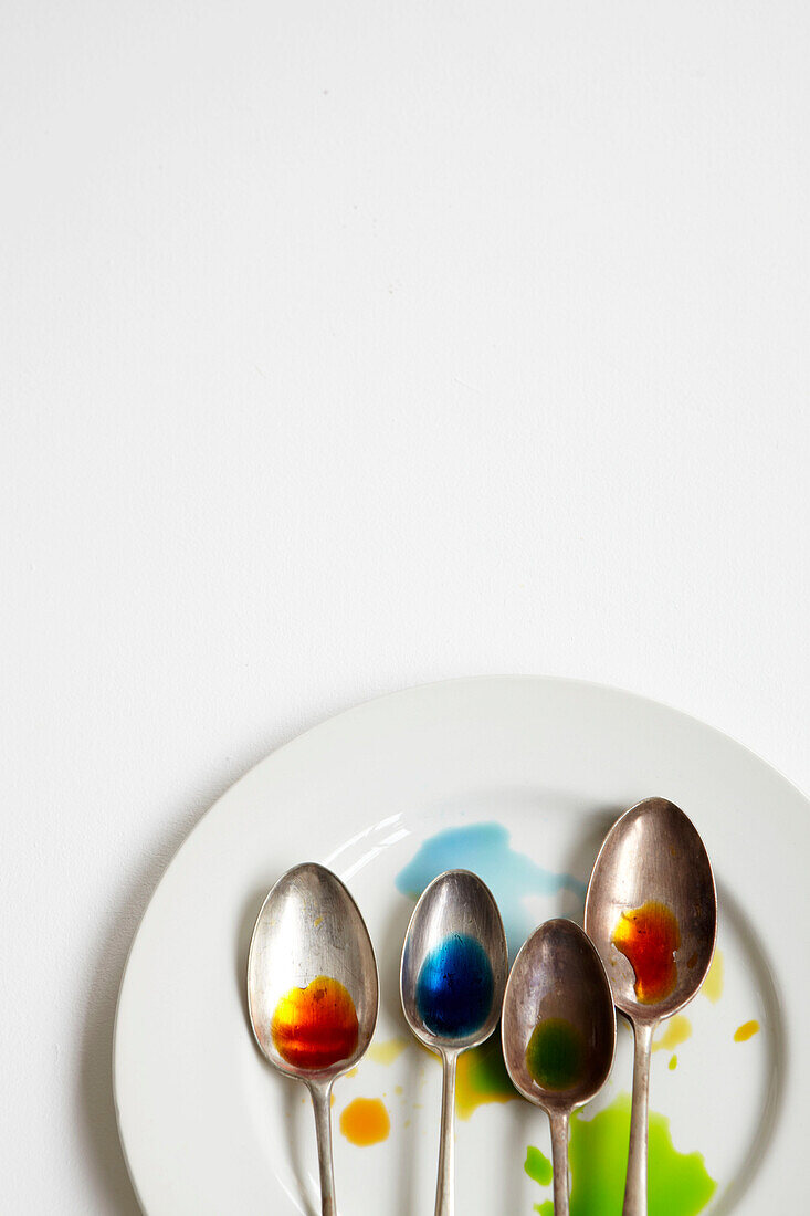 White plate with four spoons with coloured dye on