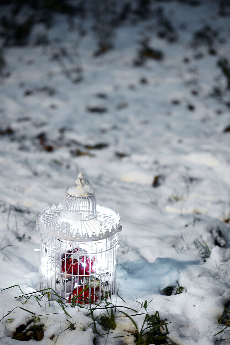White decorative birdcage filled with christmas decorations on a snowy ground