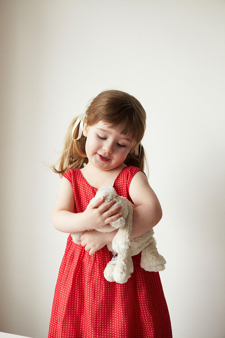 Junges Mädchen in rotem Kleid hält einen Teddybär