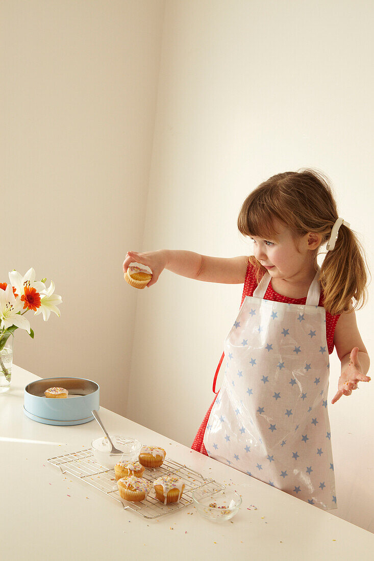 Three year old girl stands holding a fairycake with a cooling tray