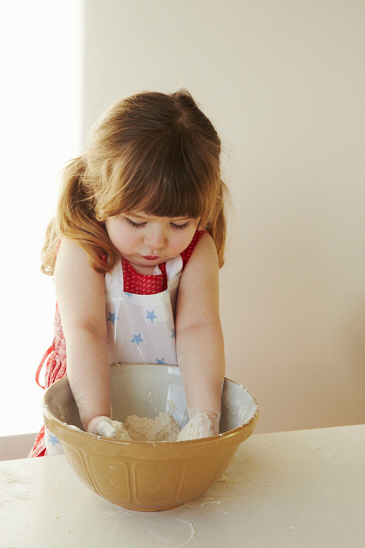 Young girl in red dress stands mixing flour in a bowl