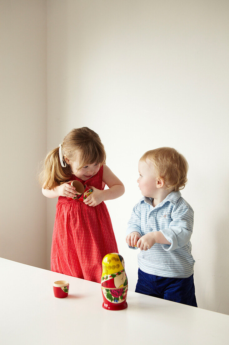 Young girl in red dress showing Russian doll to her brother