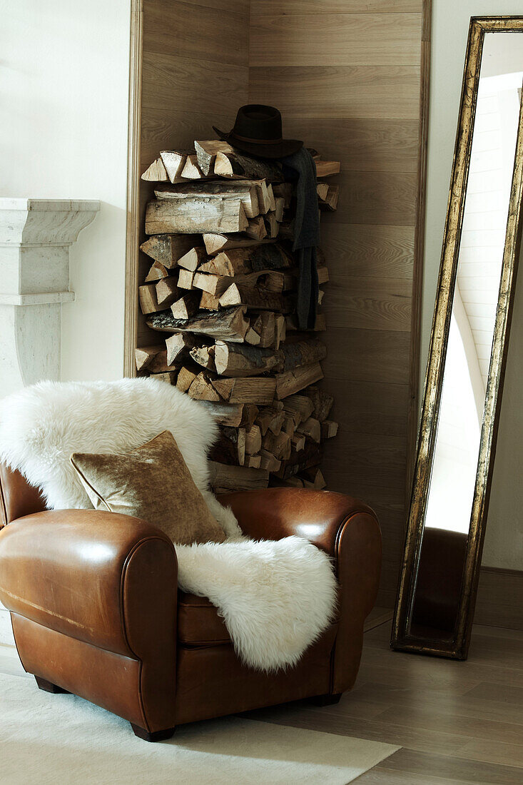 Brauner Ledersessel mit Fellüberwurf, schmalem vergoldetem Spiegel und einem Stapel Brennholz in einem luxuriösen Haus in Zermatt, Schweiz