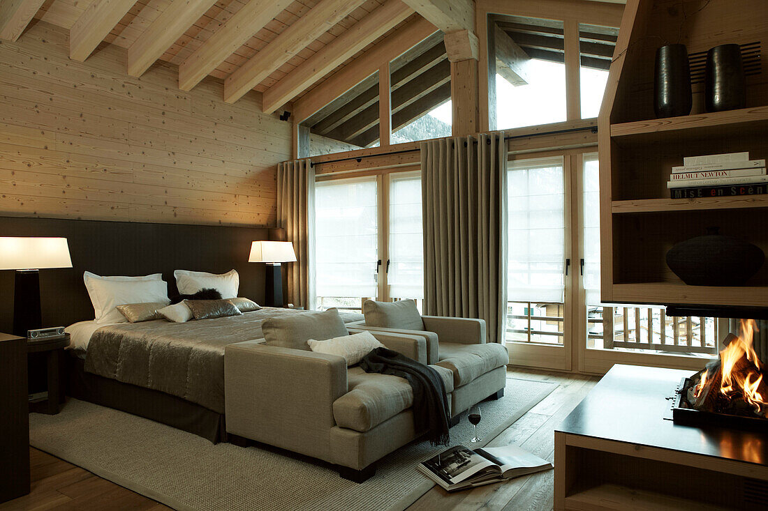 Double bed with matching lamps and armchairs in bedroom with open fire in luxury Zermatt home, Switzerland