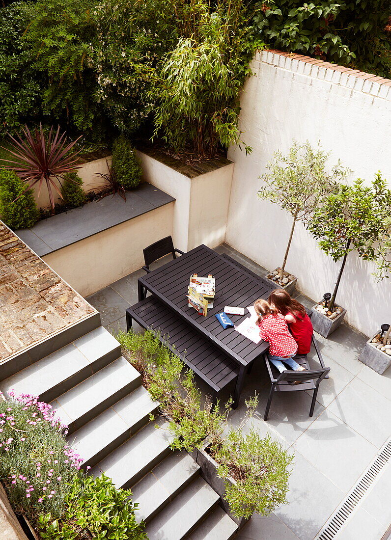 Erhöhte Ansicht von zwei Mädchen, die im Innenhof einer Terrasse an einem Tisch sitzen, London, England, UK