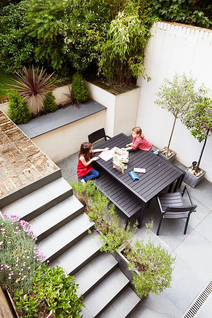 Erhöhte Ansicht von zwei Mädchen, die im Innenhof einer Terrasse an einem Tisch sitzen, London, England, UK