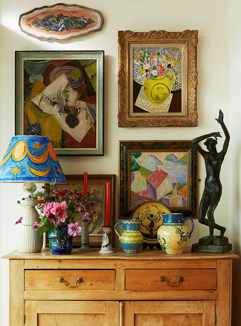 Buntes Kunstwerk und Keramik mit Statue und Lampe auf hölzernem Sideboard in einem Haus in London, England, UK