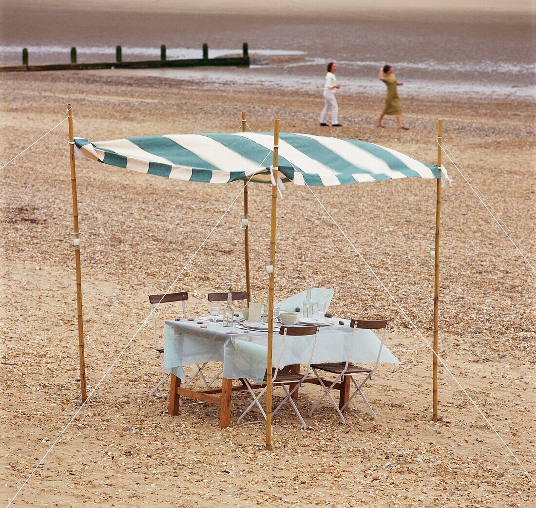 Table and chairs set on beach under striped canopy