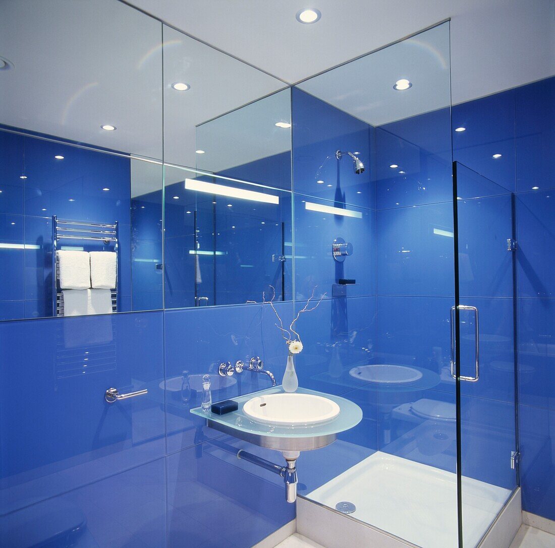 Blaues Badezimmer mit raumspiegelndem Spiegel und Glasduschkabine
