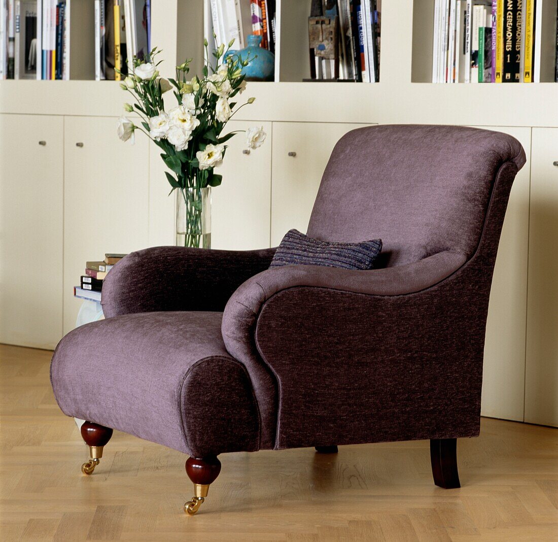 Purple armchair and vase of flowers in front of bookcase with storage cupboards