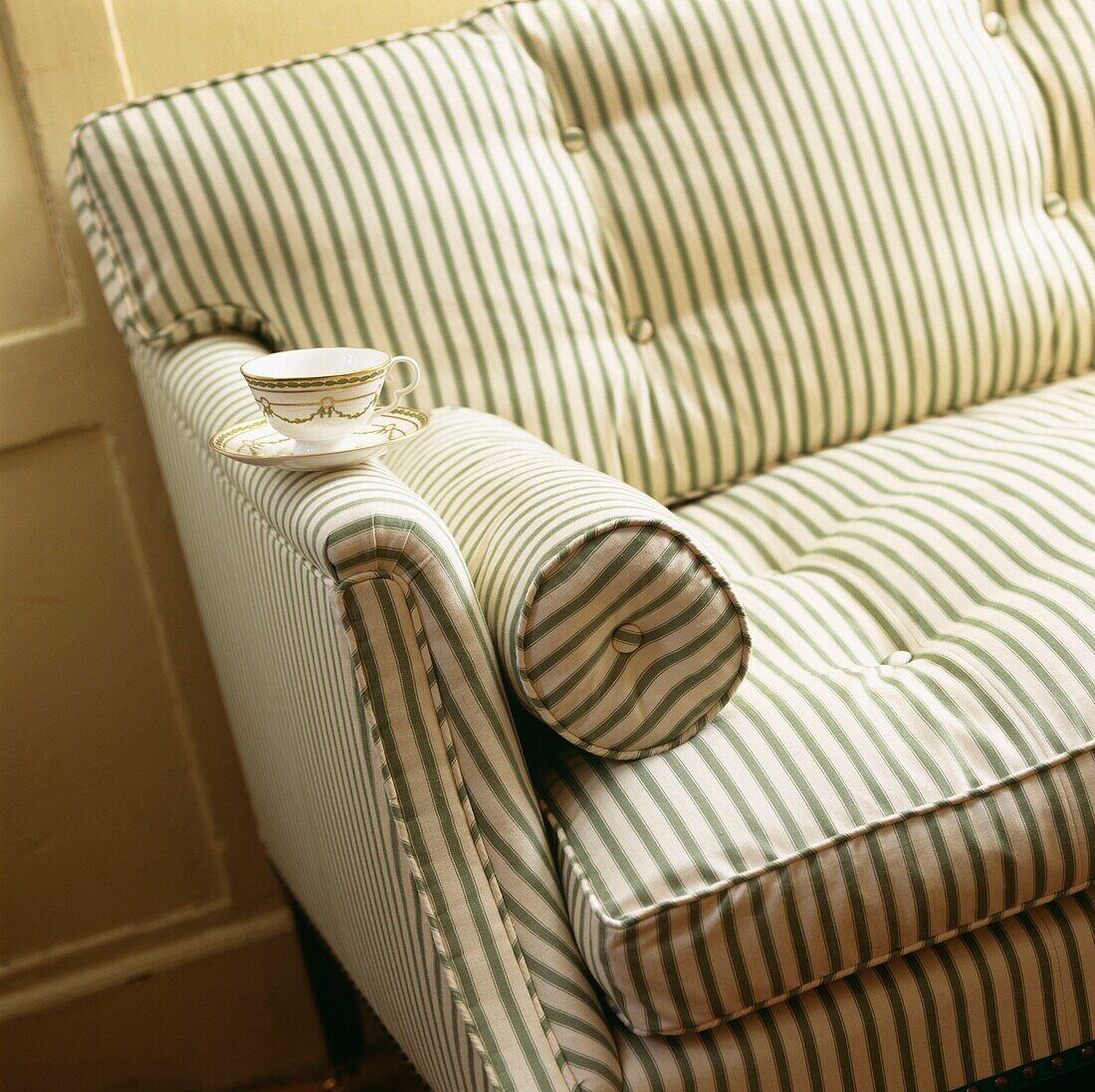 Teacup and saucer balance on arm of striped sofa with matching bolster