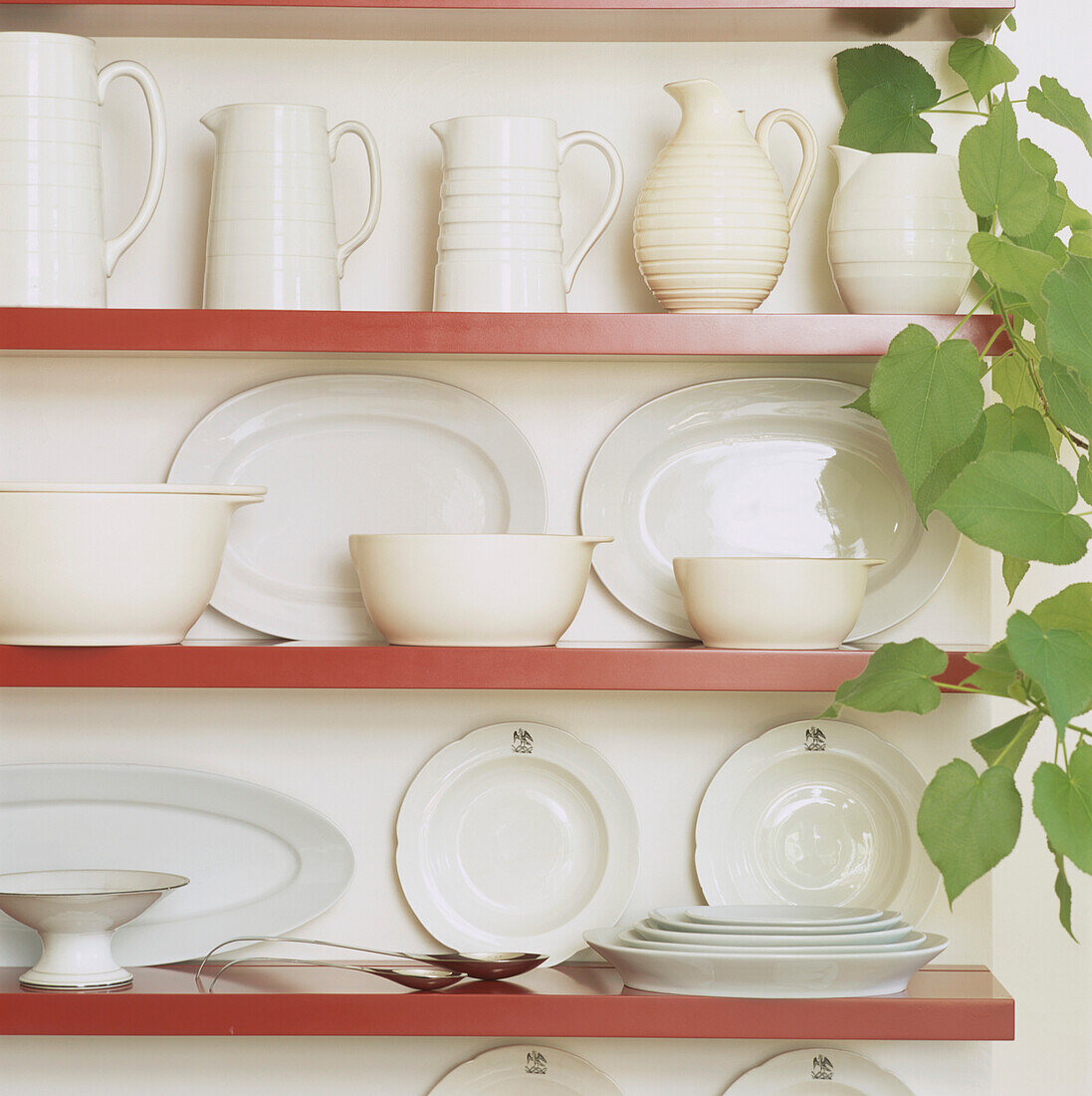 White jugs and dinner service on red lacquered shelving  