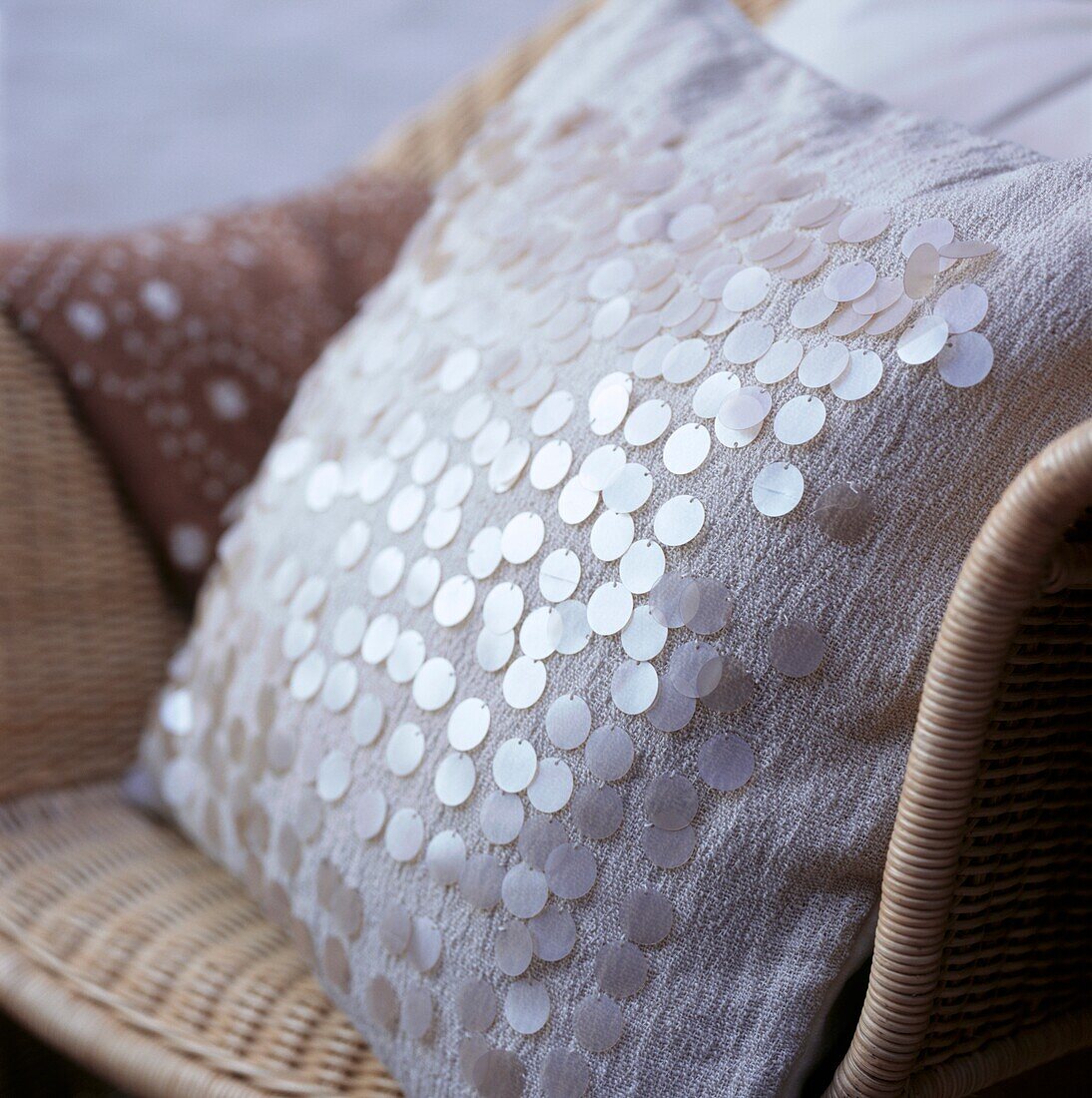 Sequinned cushion covers on woven rattan armchair