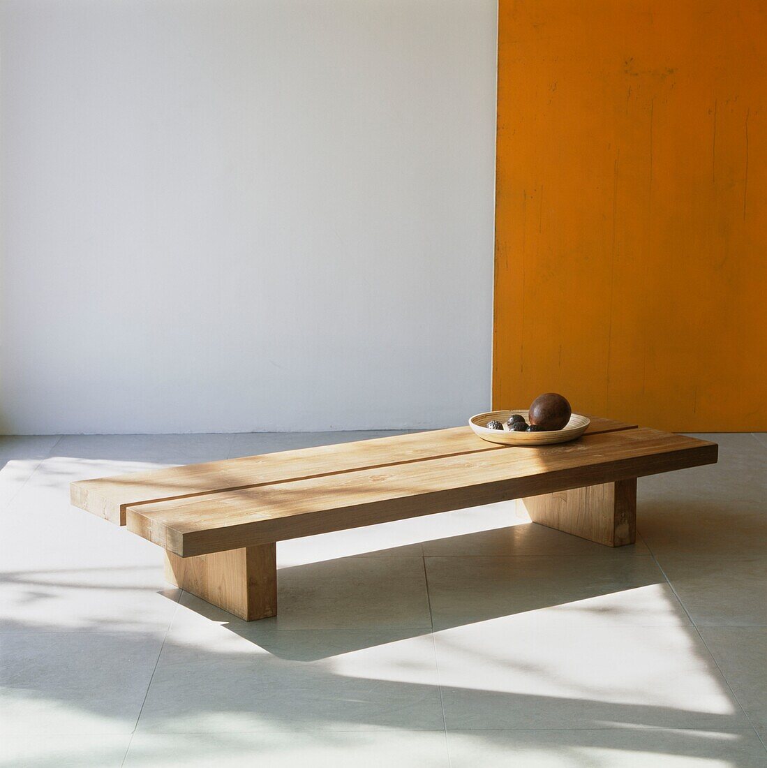 Chunky wooden coffee table with wooden dish on stone tiled floor with orange wall