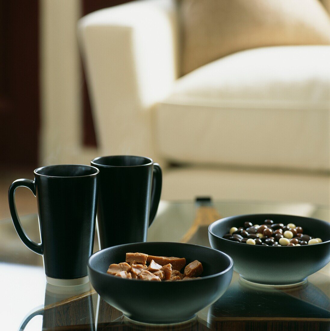 Zwei Tassen mit Schalen mit Konfekt auf einem Couchtisch mit Glasplatte