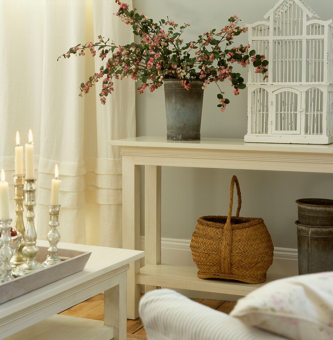 Cut flowers and birdcage on console with basket and lit candles on side table