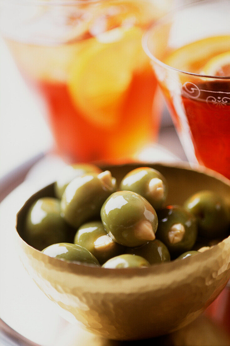 Round tray with a bowl of green olives stuffed with almonds and two glasses of pink gin in the background