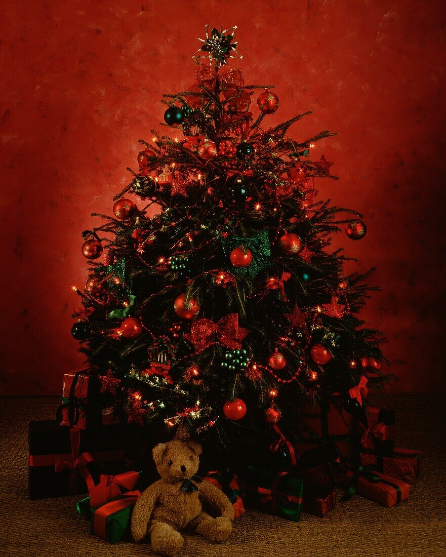 Teddybär und eingepackte Geschenke unter dem rot geschmückten Weihnachtsbaum