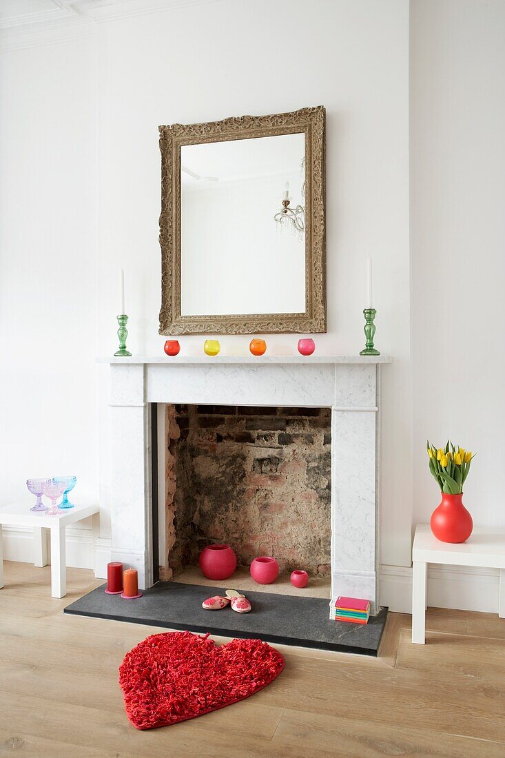 White room with marble fire surround and large mirror above the mantlepiece with colourful accessories
