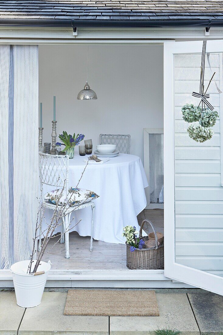 Blick in ein weißes Gartenhaus mit rundem Tisch und Stuhl