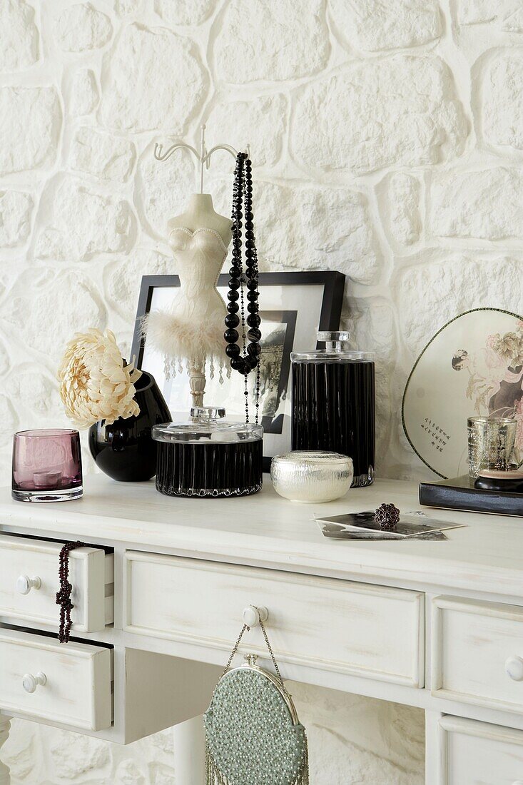 Close up of white dressing table with deco style black glass lidded jars and jewellery stand with jet beads