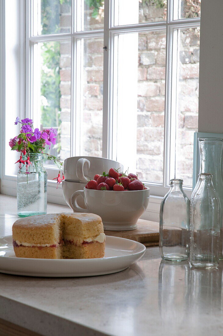 Sponge cake and strawberries with empty milk bottles on kitchen worktop in Kingston home,  East Sussex,  England,  UK