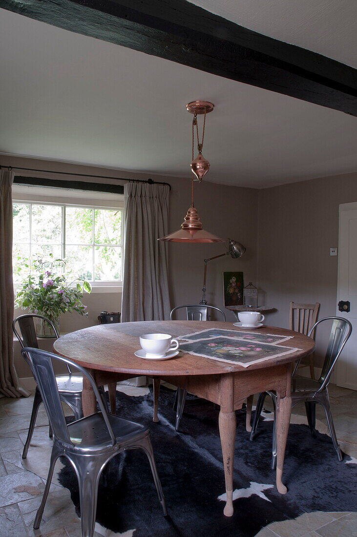 Wooden circular dining table with metal chairs under brass pendant light Kingston home,  East Sussex,  England,  UK