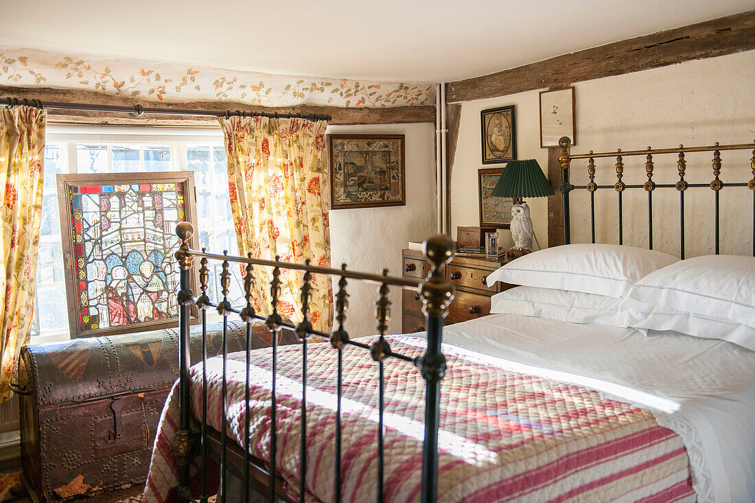 Metallbett mit genieteter Reisetruhe unter dem Fenster in einem Ashford-Bauernhaus in Kent, Großbritannien