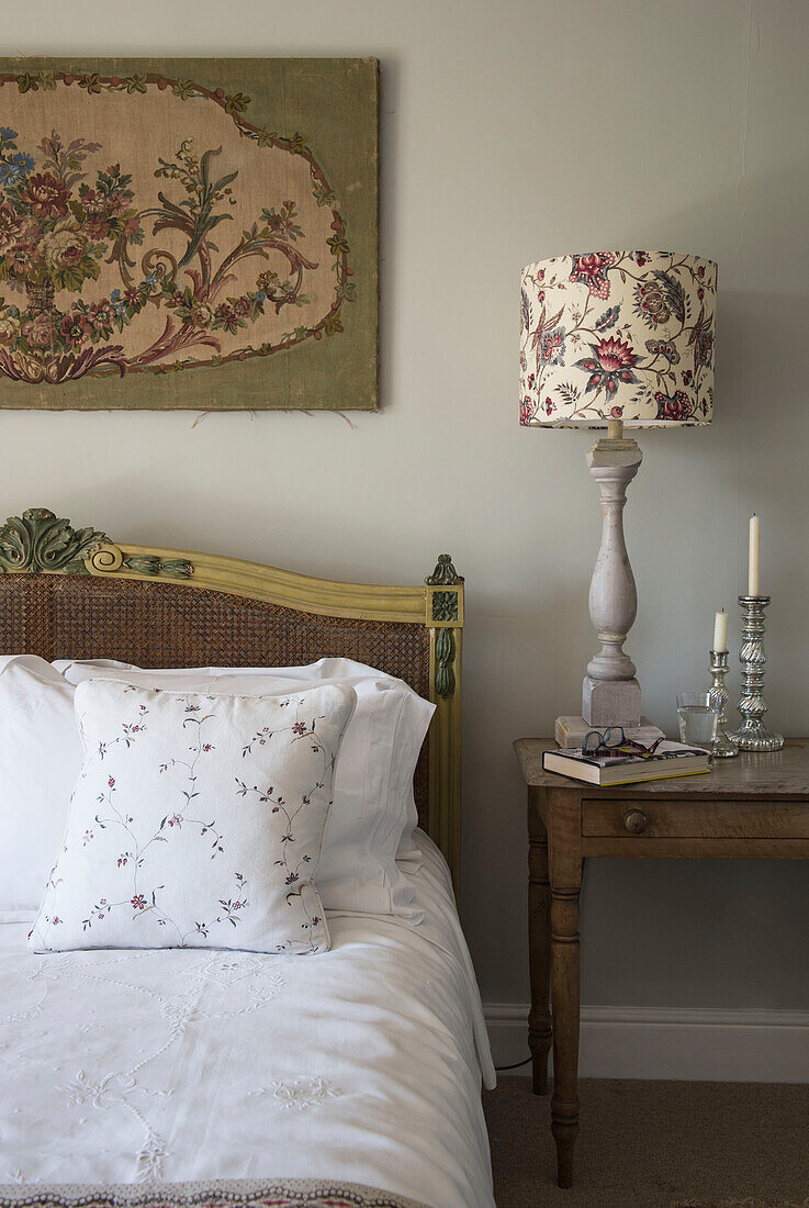 Tapestry and floral lamp with silver candlesticks at bedside in East Barsham cottage  Norfolk  England  UK