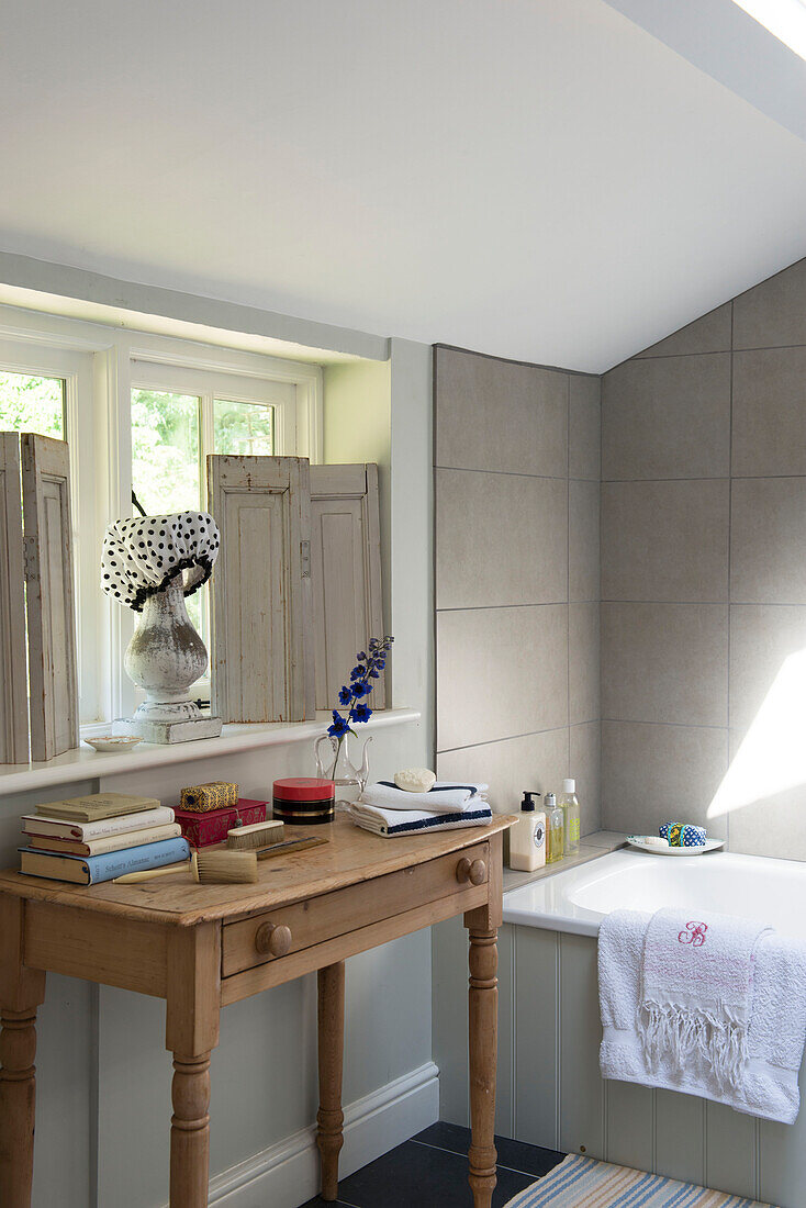 Shower cap and shutters on windowsill with wooden table in bathroom of East Barsham cottage  Norfolk  England  UK