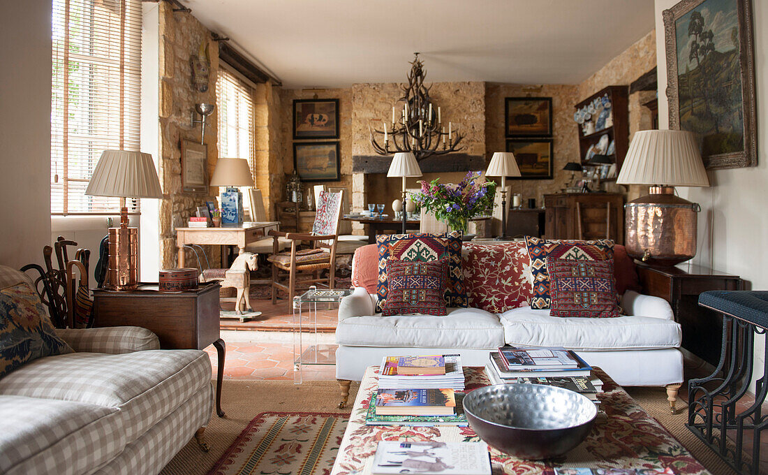 Metallschüssel und Zeitschriften auf Ottomane mit Gobelin-Kissen im offenen Wohnzimmer eines Landhauses in der Dordogne in Frankreich