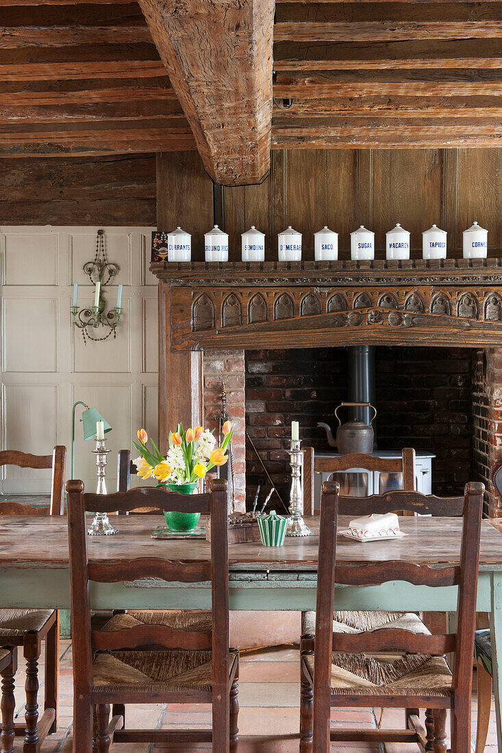 Esszimmerstühle am Tisch mit geschnitztem Kamin unter Balkendecke in einem Haus in Suffolk, England, Vereinigtes Königreich