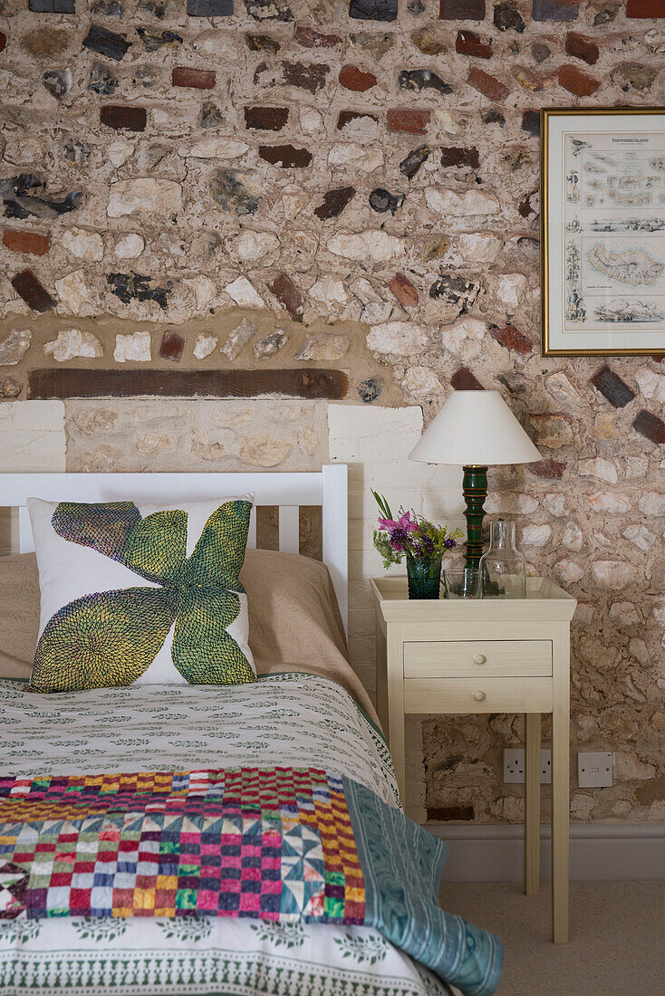 Patchwork auf einem Doppelbett mit freiliegender Steinwand in einer umgebauten Scheune in Norfolk aus dem 18