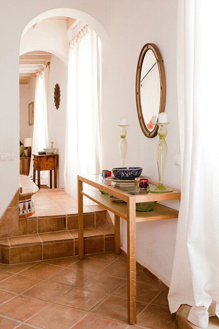 Glass candlesticks on console with oval mirror in terracotta tiled hallway, Castro Marim, Portugal