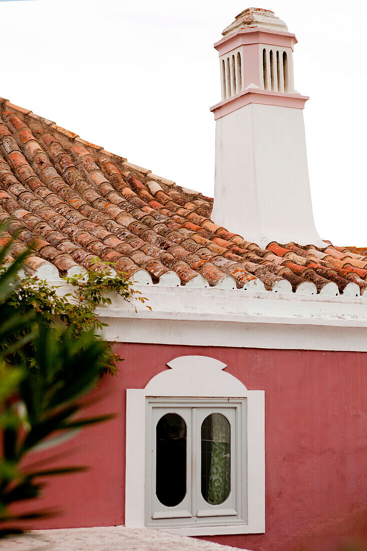 Tiled roof and chimney with window set in red walls of Castro Marim home, Portugal
