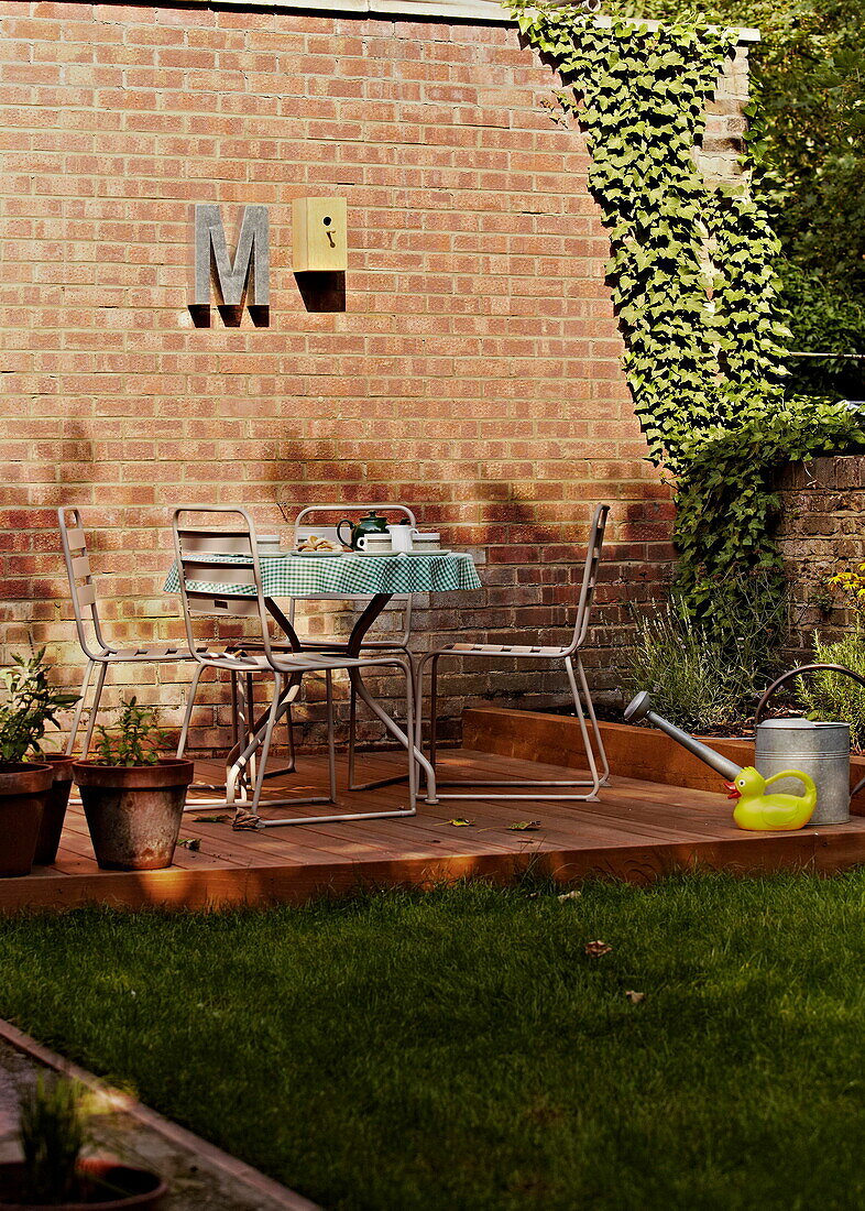 Decked terrace with table and chairs in walled garden exterior of London family home  England  UK