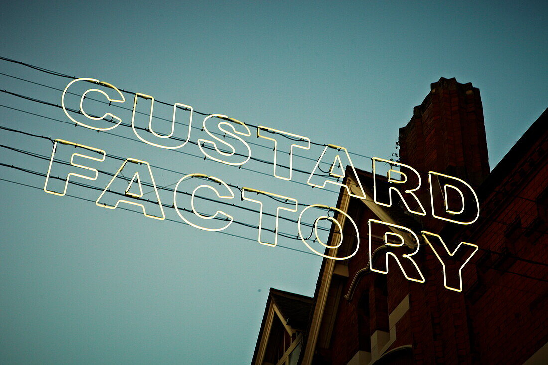 Großer Schriftzug 'CUSTARD FACTORY' in Neonlicht vor einem Wohnhaus in Birmingham UK