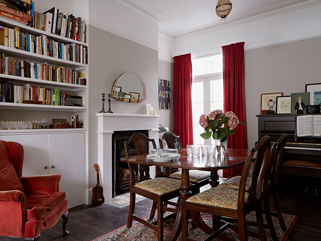 Polished dining table and bookshelves with red velvet curtains and armchair in contemporary London home   England   UK