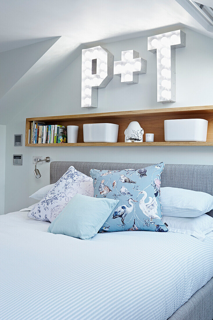 Bird patterned cushion on double bed below wooden shelf with letters 'P' and 'T' of London townhouse  England  UK