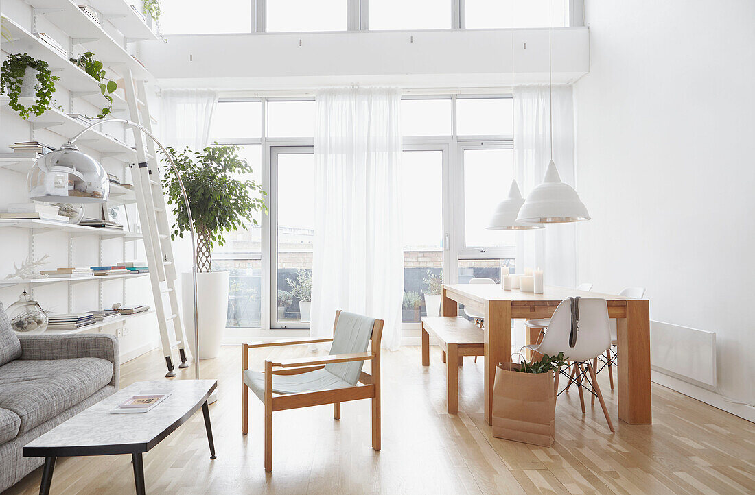 Dining table and shelves with ladder in open plan living room of London home  UK