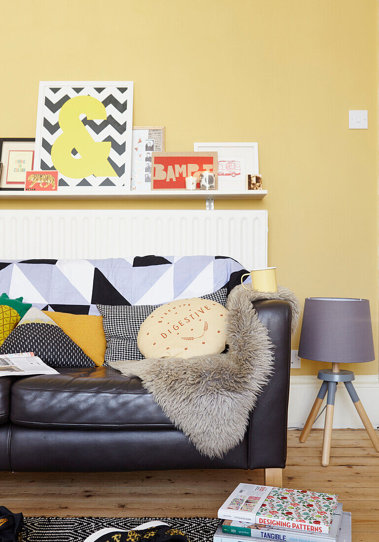 Assorted cushions on black leather sofa in yellow living room of Alloa home  Scotland  UK