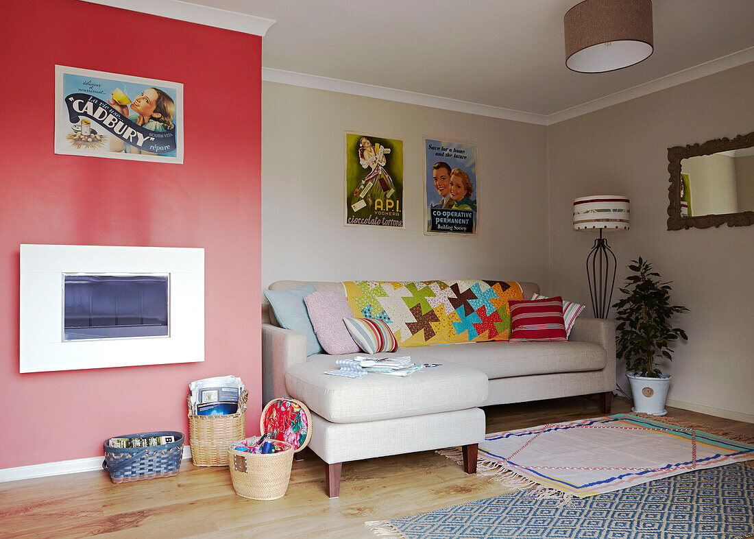 Rote Wand mit Print-Kollektion und bunten Kissen im Wohnzimmer eines Hauses in Bolton, Greater Manchester, England, UK