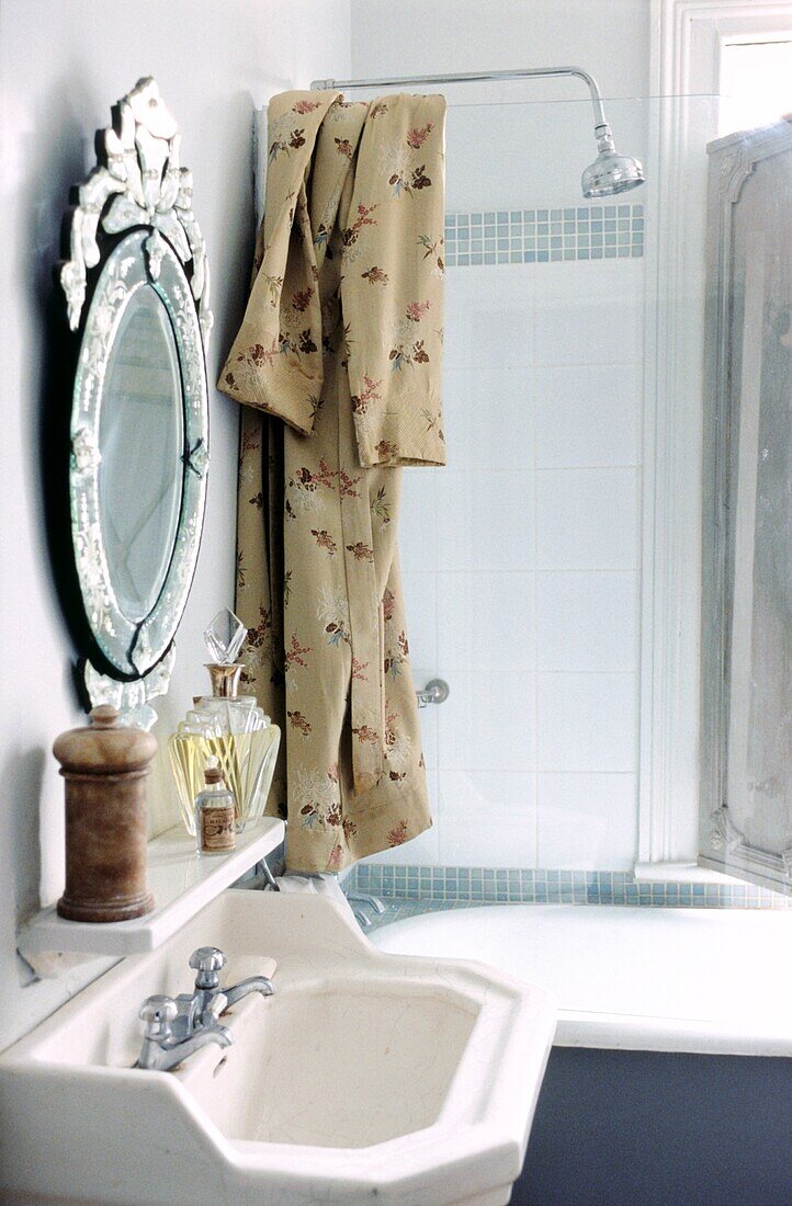 Detail of bathroom with hand basin and shower over roll top bath