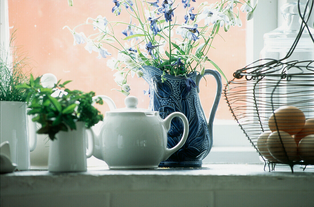 Auslage von Geschirr und Küchenutensilien mit Kräutern und Blumen