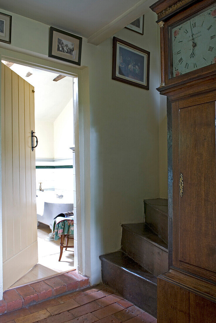 Offene Tür zum Badezimmer vom Flur mit Holztreppe und Standuhr