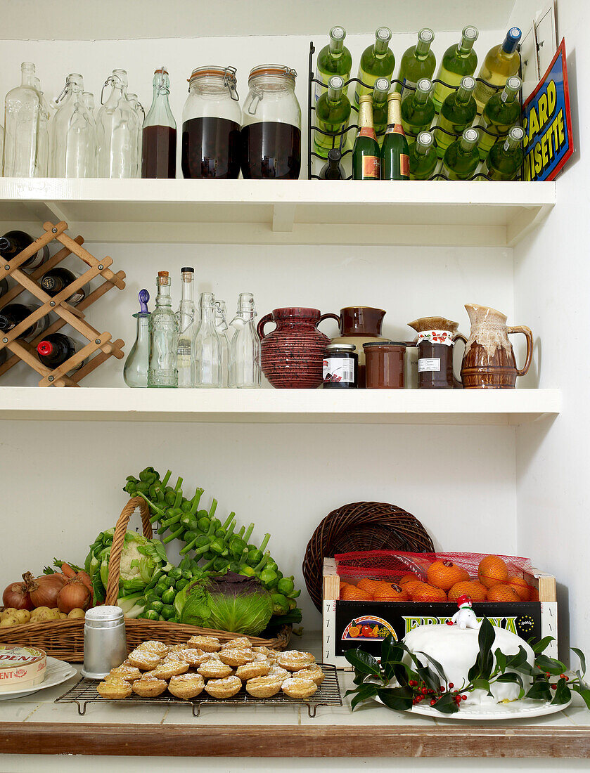Close up of pantry filled with wine bottles mince pies fruit and vegetables and a christmas cake