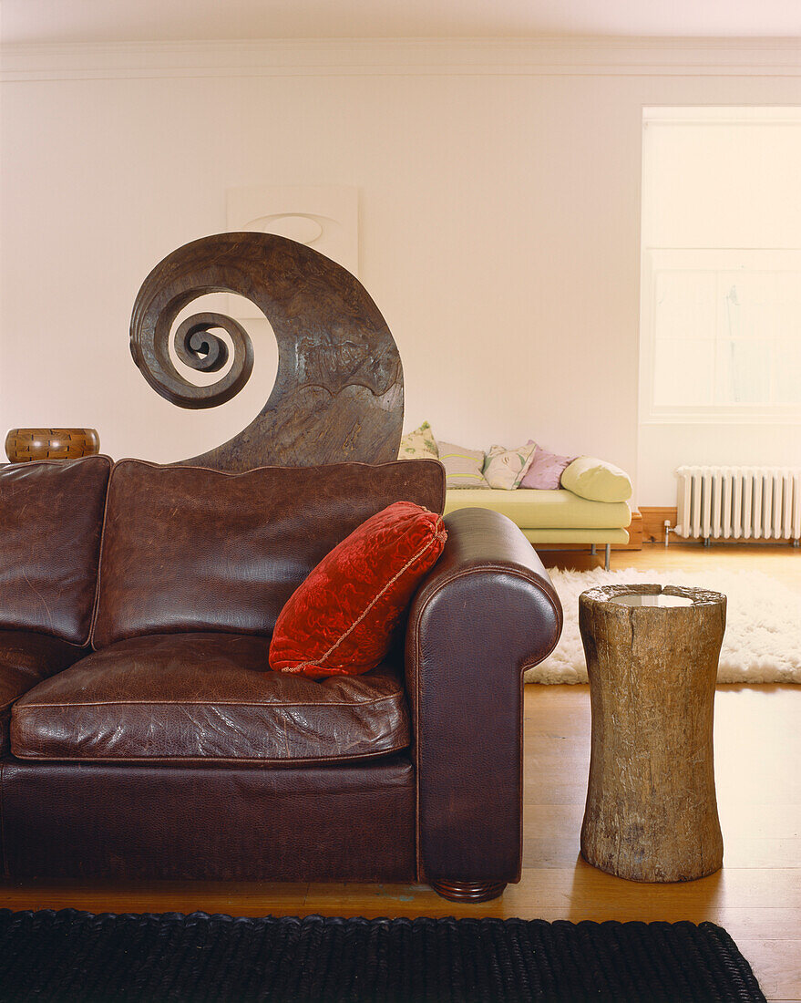 Leather sofa with prow of a Keralan canoe in a living room with uncurtained windows